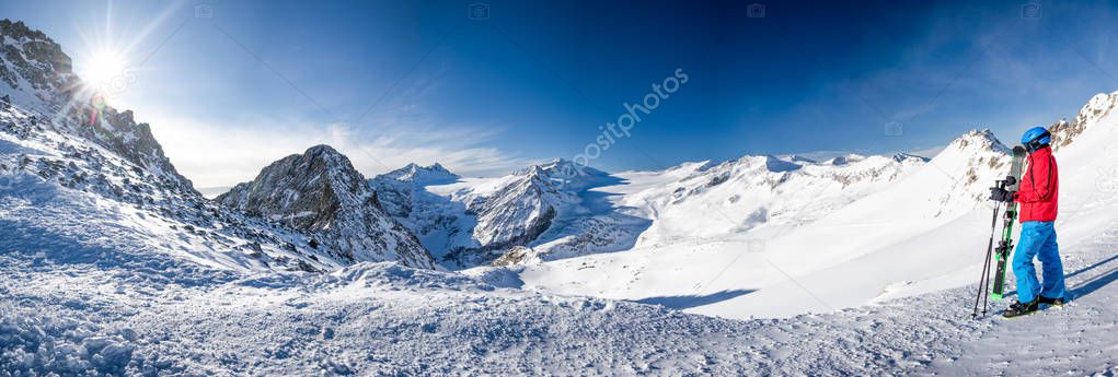 Young happy skier sitting on the top of mountains and enjoying view of Rhaetian Alps from Presena Glacier, Tonale pass, Italy, Europe.  