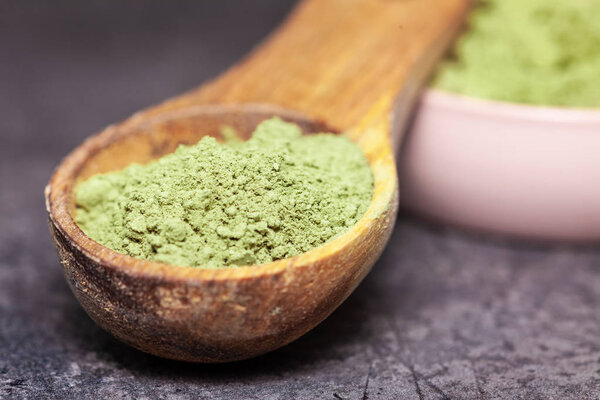 Порошковый маття в миске и деревянной ложке на темном фоне - альтернатива медицине
