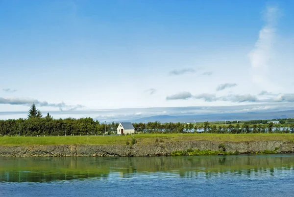 Küçük geleneksel ev, nehir ve arkasında dağlar ile İzlanda manzara.
