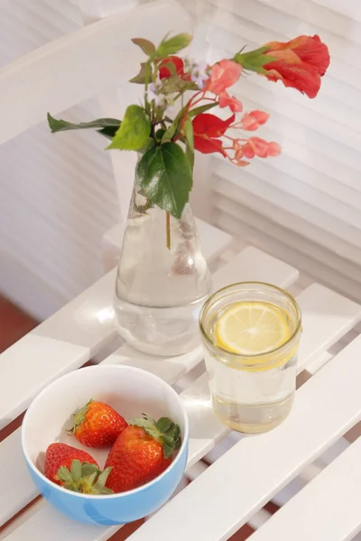 Soda camlı ve limon dilimili bir sandalye. Ayrıca çilek ve silvester çiçekleri. Güneşli bir günde beyaz arka plan.