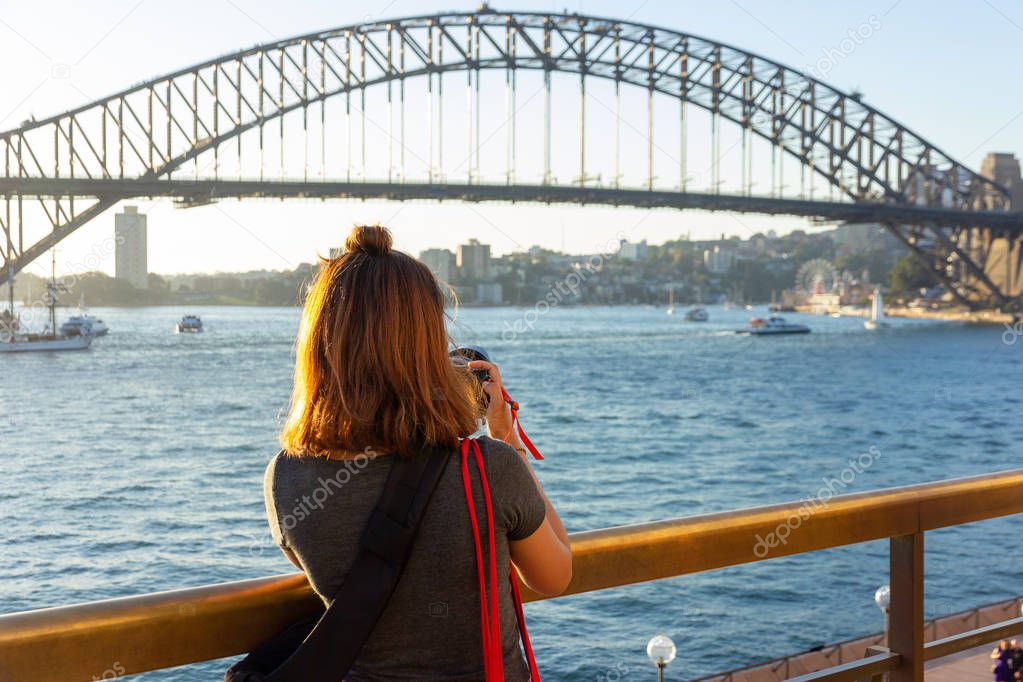 Female tourist with backpack bag  taking photos of Sydney Harbour Bridge during summer vacation trip.