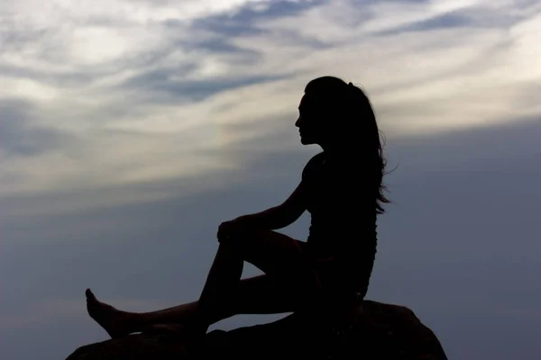 Silhouettes of Female tourist  sitting on top rock with twilight sky at sunset.