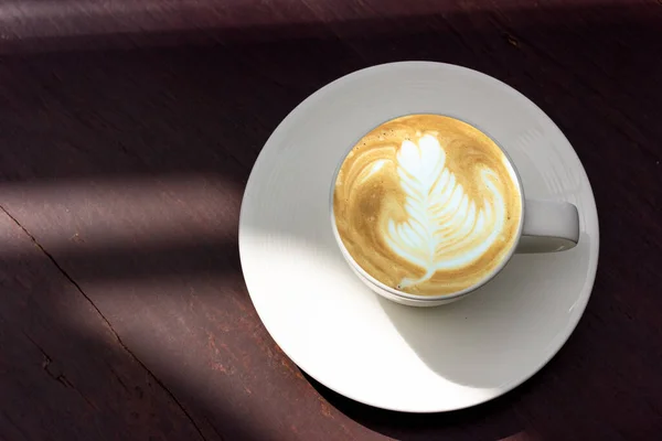 Kahverengi ahşap masada, fotokopi alanı ile şekillendirilmiş, beyaz latte sanat kahvesi..