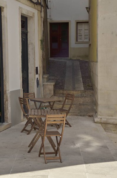 Wooden table and chairs at corner in cobbled alley in the old town of Coimbra, Portugal.
