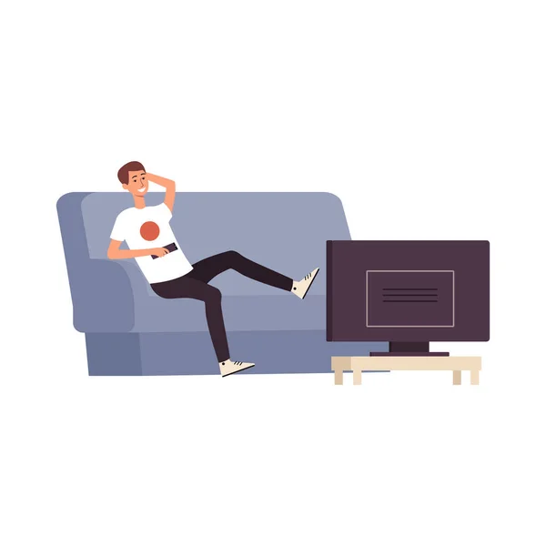 Jovem sorri e se senta em um sofá ou sofá com um controle remoto na mão e assiste TV . —  Vetores de Stock