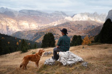 Dağlardaki vadide köpekli şapkalı bir adam. Nova Scotia Duck Tolling Retriever. # Erkekler kayalıklarda otururlar #