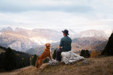 Dağlardaki vadide köpekli şapkalı bir adam. Nova Scotia Duck Tolling Retriever. # Erkekler kayalıklarda otururlar #