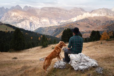 Dağlardaki vadide köpekli şapkalı bir adam. Nova Scotia Duck Tolling Retriever. # Erkekler kayalıklarda otururlar #