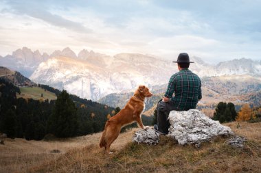 Dağlardaki vadide köpekli şapkalı bir adam. Nova Scotia Duck Tolling Retriever. # Erkekler kayalıklarda otururlar #