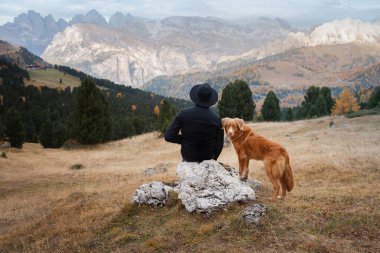 Dağlardaki vadide köpekli şapkalı bir adam. Nova Scotia Duck Tolling Retriever. # Erkekler kayalıklarda otururlar #