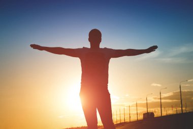 Gün batımında yükseltilmiş kollu adam silüeti