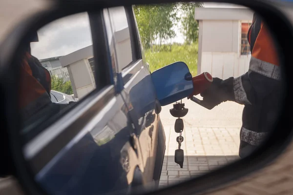 Reflection in car mirror of the man fuel the car on petrol stati