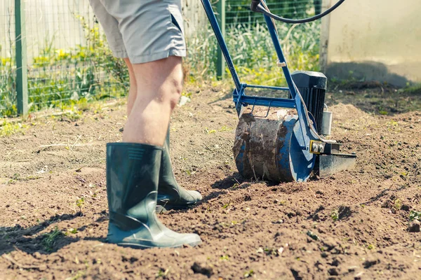 A man plows the ground in the garden with an electric cultivator