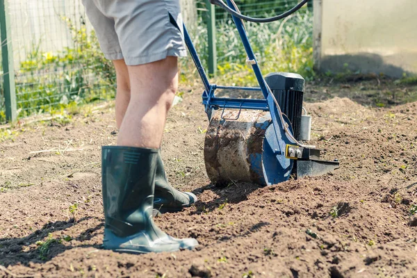 A man plows the ground in the garden with an electric cultivator