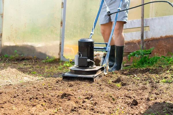 A man plows the ground in the garden with an electric cultivator.