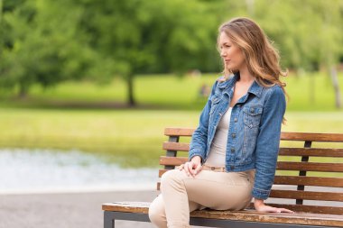 Genç bir kadın parkta bankta oturuyor.