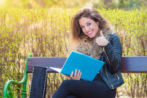 Hermosa estudiante sentada en un banco en el parque y aprendiendo —  Fotos de Stock