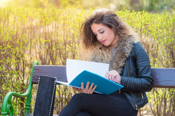 Schöne Studentin sitzt auf einer Bank im Park und lernt — Stockfoto