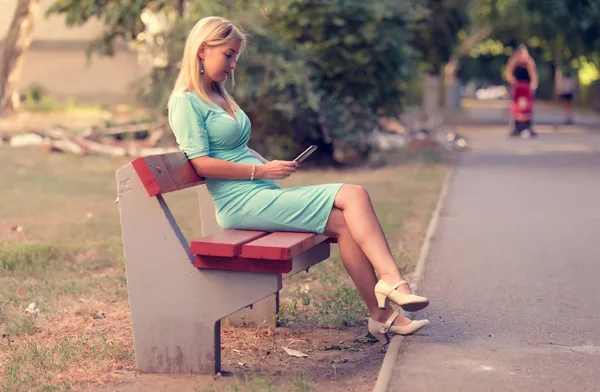 Cute woman sitting on the bench and use her phone — Stock Photo, Image