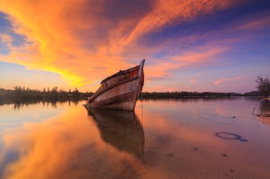 Sahildeki eski enkazı terk et, Borneo, Gün batımını yansıtan eski balıkçı teknesi