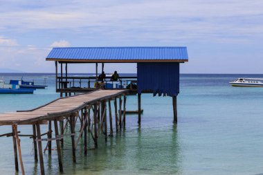 Mantanani Adası, Kuzey Borneo 'da mavi gökyüzü okyanusu ve yeşil okyanusla uzun ahşap iskele ve beyaz kumsal manzarası.