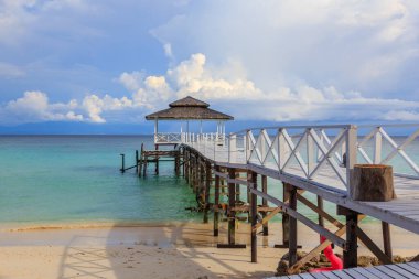 Mantanani Adası, Kuzey Borneo 'da mavi gökyüzü okyanusu ve yeşil okyanusla uzun ahşap iskele ve beyaz kumsal manzarası.