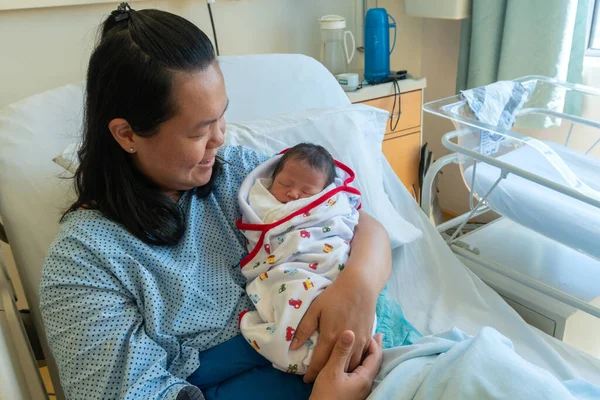 Happy Asia Chinese Mother holding her newborn child after labor in hospital wad room