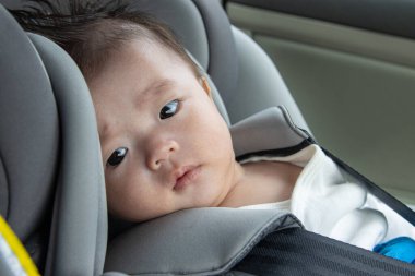 Yerel yaşam tarzı Asyalı Çinli bebek mutlu gülümseyen beyaz çocuk emniyet oto koltuğuna oturur.