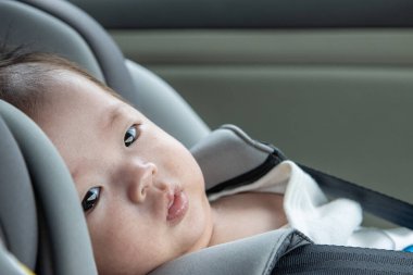 Yerel yaşam tarzı Asyalı Çinli bebek mutlu gülümseyen beyaz çocuk emniyet oto koltuğuna oturur.