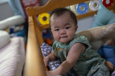 Sevimli bebek beşikte oturuyor ve oyuncaklarla oynuyor.