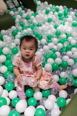 Sevimli küçük kız top havuzunda oynarken gülümsüyor.