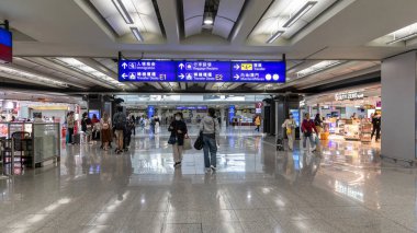 Hong Kong, Çin: 21 Mart 2024: Koruyucu yüz maskesi takan yolcular havaalanı terminalinde navigasyon işaretleriyle yürüyorlar