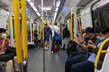 Hong Kong, Çin - 21 Mart 2024: Yüz maskesi takan yolcular akıllı telefonlarını kullanırken metroya biniyorlar