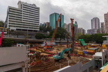 Hong Kong, Çin - 22 Mart 2024: Yoğun bir şehir merkezinde, arka planda modern ofis kuleleri bulunan bir inşaat alanında ağır makineler kullanan inşaat işçileri