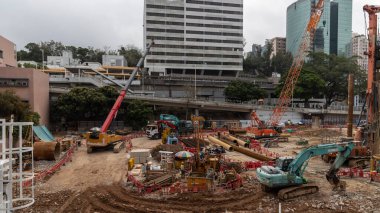Hong Kong, Çin - 22 Mart 2024: Yoğun bir şehir merkezinde, arka planda modern ofis kuleleri bulunan bir inşaat alanında ağır makineler kullanan inşaat işçileri