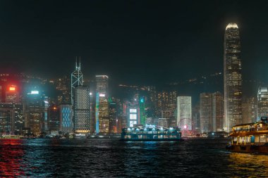 Hong Kong, Çin - 22 Mart 2024: Hong Kong gökdelenleri Victoria Limanı 'ndan geçen binaların ve teknelerin ışık huzmeleriyle gece parlıyor