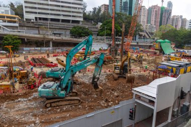 Hong Kong, Çin - 22 Mart 2024: Yoğun bir şehir merkezinde, arka planda modern ofis kuleleri bulunan bir inşaat alanında ağır makineler kullanan inşaat işçileri