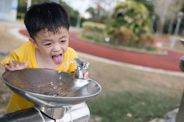 Мальчик высовывает язык, когда пьет воду из питьевого фонтана в жаркий день.