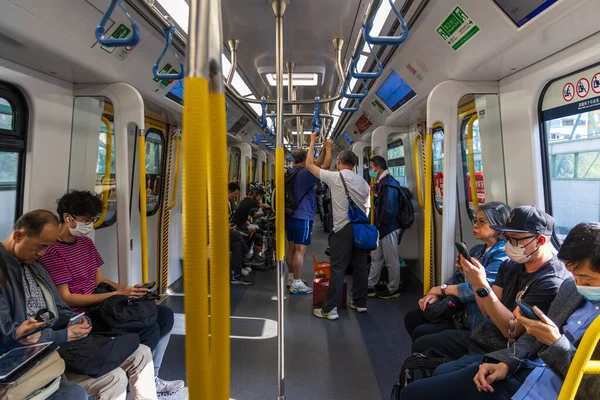 Hong Kong, Çin - 21 Mart 2024: Yüz maskesi takan yolcular akıllı telefonlarını kullanırken metroya biniyorlar