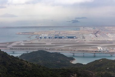 Terminale parketmiş uçaklar ve ön plandaki su üzerinde köprü olan yoğun bir havaalanının havadan görüntüsü.