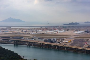 Hong Kong, Çin - 23 Mart 2024: Yoğun bir havaalanının ön planda su üzerinde köprü ve terminale park edilmiş uçakları görüntüsü