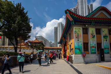 Hong Kong, Çin - 24 Mart 2024: Hong Kong, Çin 'de yüksek binaları olan renkli bir tapınağın yanındaki kaldırımda yürüyen turistler