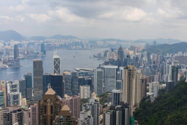 Hong Kong, Çin - 25 Mart 2024: Hong Kong siluetinin nefes kesici manzarası, şehrin etkileyici gökdelenlerinin limanın ve etrafındaki dağların yükselişini gözler önüne seriyor