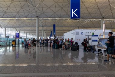 Hong Kong, Çin - 26 Mart 2024: kalabalık havaalanı terminali gişede kayıt için sırada bekleyenler var. Bavulu olan yolcular modern bir şekilde uluslararası uçuşlara hazırlanıyorlar..