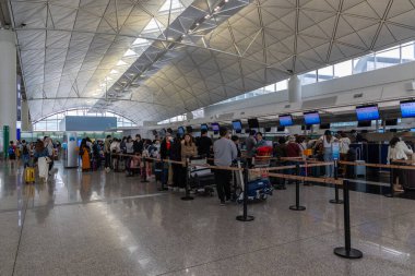 Hong Kong, Çin - 26 Mart 2024: kalabalık havaalanı terminali gişede kayıt için sırada bekleyenler var. Bavulu olan yolcular modern bir şekilde uluslararası uçuşlara hazırlanıyorlar..