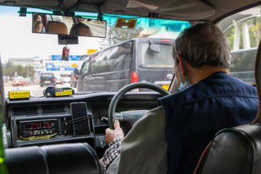Hong Kong, Çin - 21 Mart 2024 Kıdemli taksi şoförü yüz maskesi takıyor ve yolcularını Hong Kong 'un işlek sokaklarında gezdiriyor.