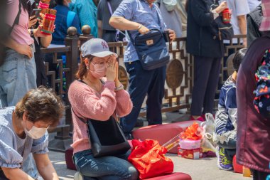 Hong Kong, Çin - 24 Mart 2024: Asya 'da bir tapınakta diz çöküp tütsü çubuklarıyla dua eden cerrahi maske takan Asyalı kadın
