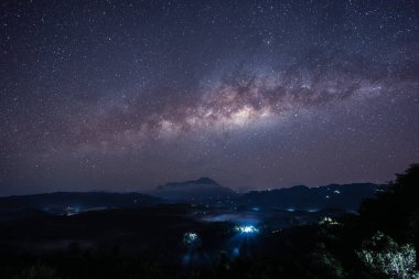 Samanyolu galaksisi bir dağın tepesinde parıldıyor ve turistler geceleri bir orman tepesinden bizi izliyor.