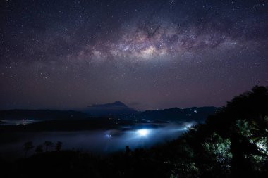 Samanyolu galaksisi bir dağın tepesinde parıldıyor ve turistler geceleri bir orman tepesinden bizi izliyor.