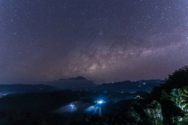 Samanyolu galaksisi bir dağın tepesinde parıldıyor ve turistler geceleri bir orman tepesinden bizi izliyor.